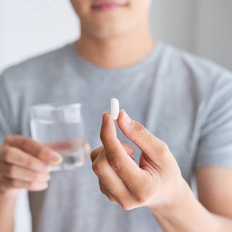Closeup of man holding a pill in one hand and glass of water in the other